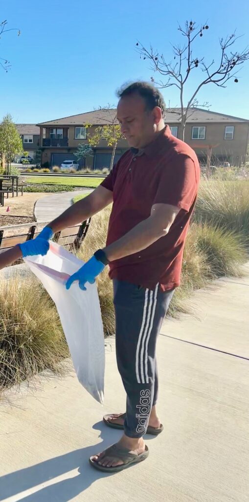 A man holds a bag of trash whole someone out of frame drops trash into it.